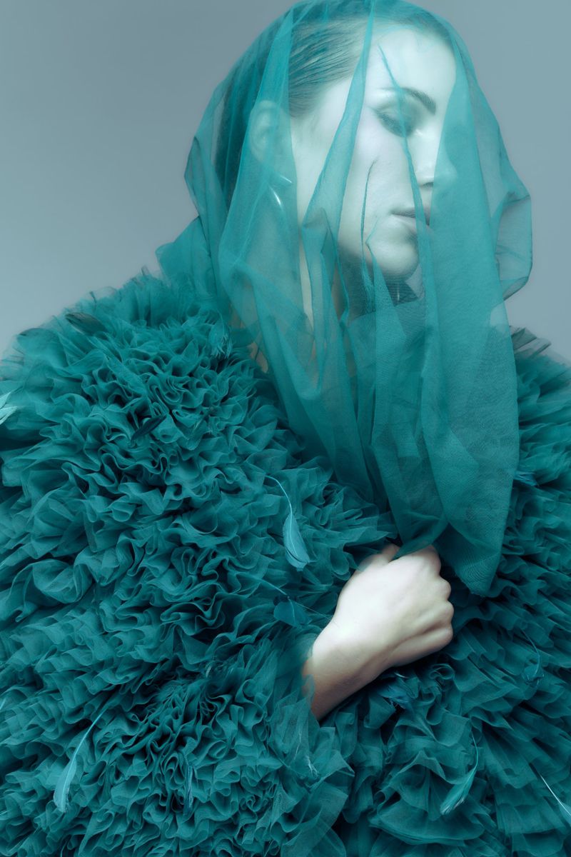 Woman with veil and ruffled emerald dress in a portrait shot. The image is softly lit and the subject's eyes are closed.