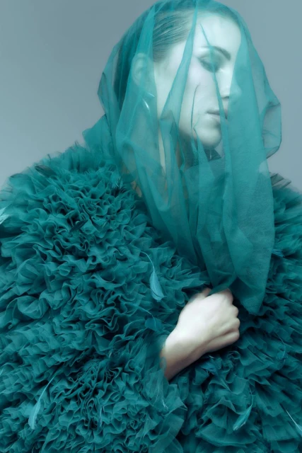 Woman with veil and ruffled emerald dress in a portrait shot. The image is softly lit and the subject's eyes are closed.