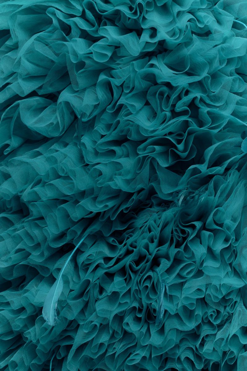 Close-up of teal fabric with ruffled texture. Abstract fabric background showcases layered, undulating ruffles with shades of teal.