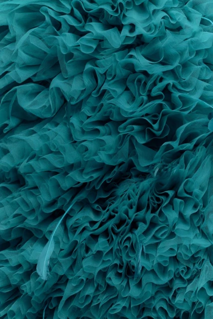 Close-up of teal fabric with ruffled texture. Abstract fabric background showcases layered, undulating ruffles with shades of teal. 