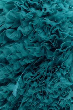 Close-up of teal fabric with ruffled texture. Abstract fabric background showcases layered, undulating ruffles with shades of teal. 