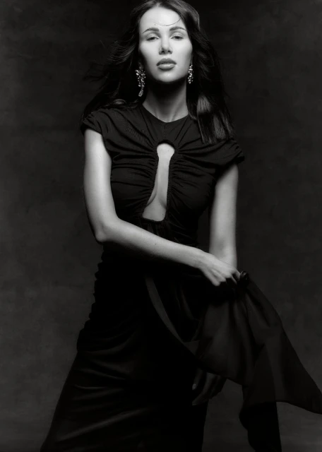 Elegant woman in a black dress poses against a dark background, showcasing fashion and portrait photography, with flowing fabric detail.