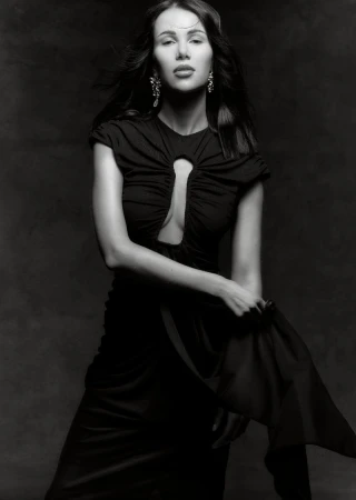 Elegant woman in a black dress poses against a dark background, showcasing fashion and portrait photography, with flowing fabric detail.
