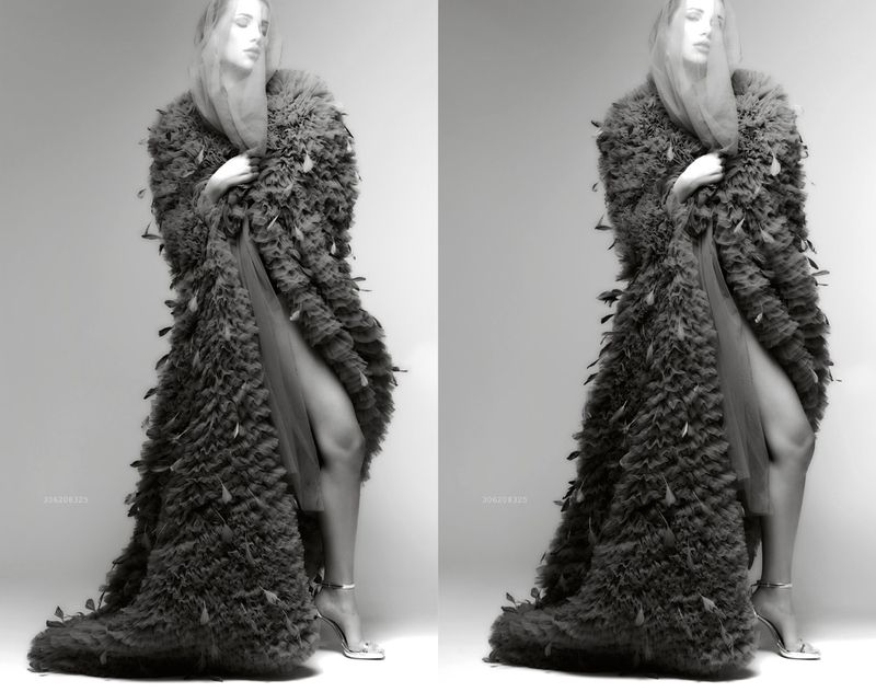 Monochrome image of a woman in a feathered coat with leg and heeled sandals visible, posing in a photo studio against a neutral backdrop.