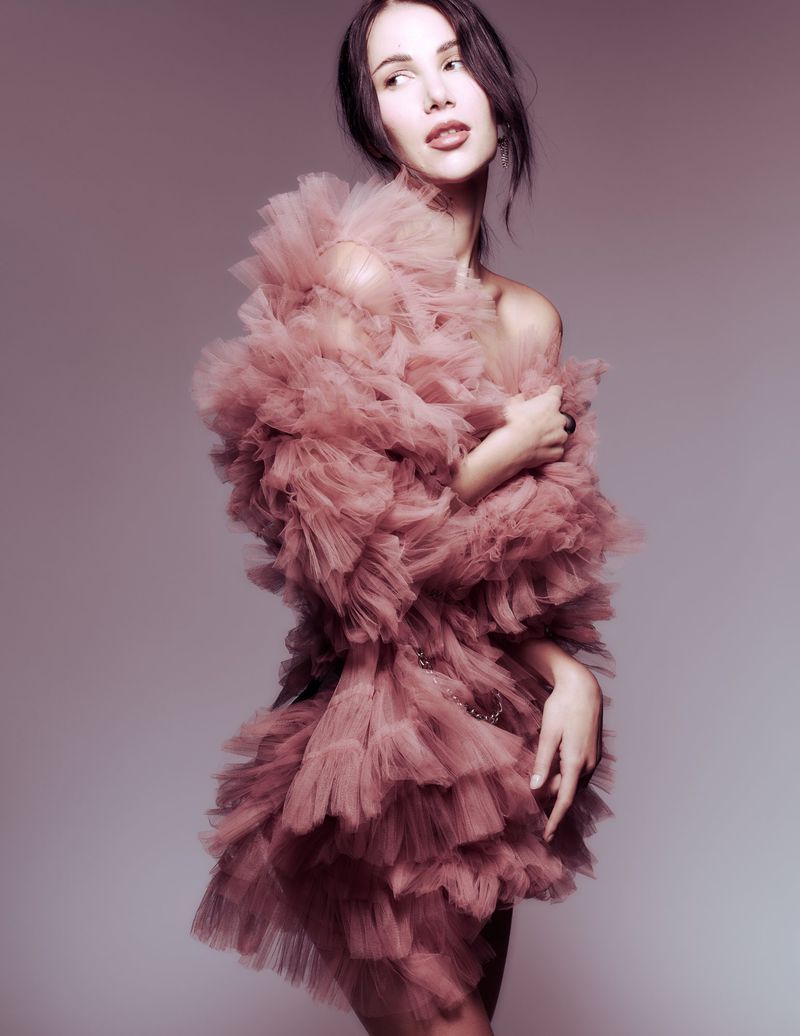 Glamorous woman in a pink tulle dress strikes a pose in a studio setting, showing off the dress's intricate ruffles and unique design.