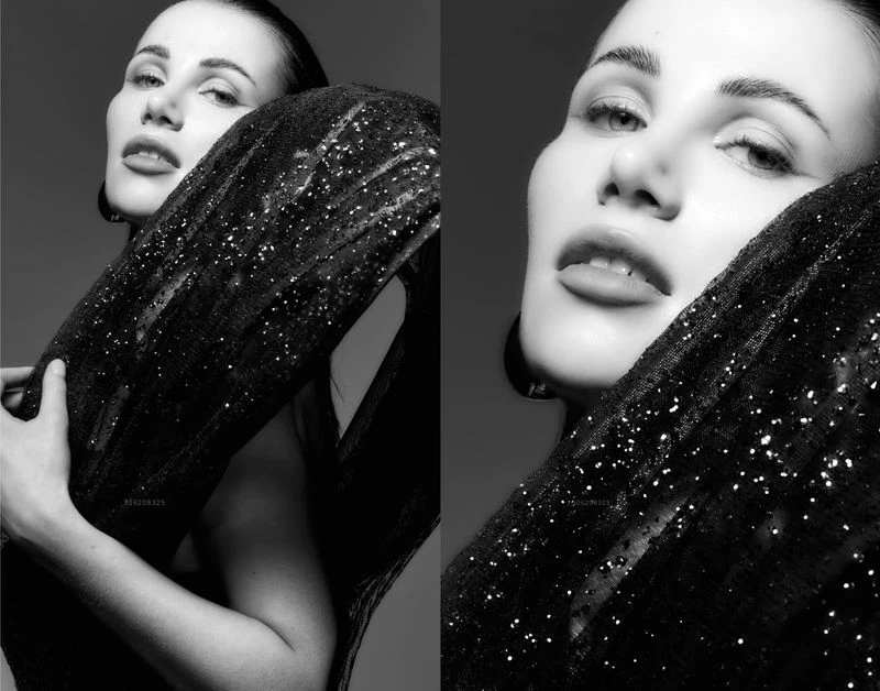 Monochrome portrait of a woman with dark hair, wearing a sparkling black dress, posing against a dark grey background in a studio.