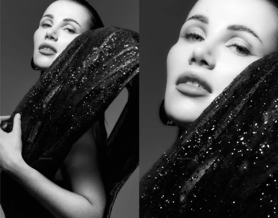 Monochrome portrait of a woman with dark hair, wearing a sparkling black dress, posing against a dark grey background in a studio.