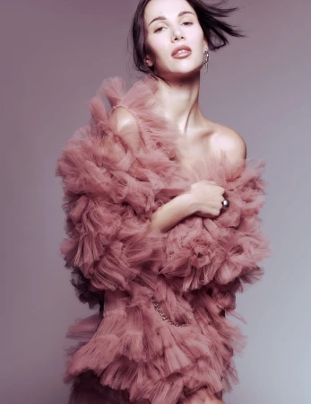 Elegant woman in a ruffled dress, posing in a studio setting with soft lighting, showcasing fashion and beauty.