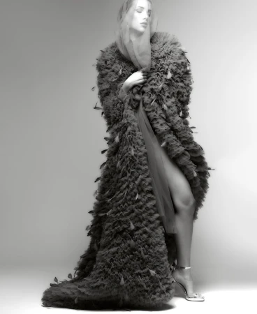 Model in textured feather coat and sheer head covering posing against a white seamless background for fashion editorial