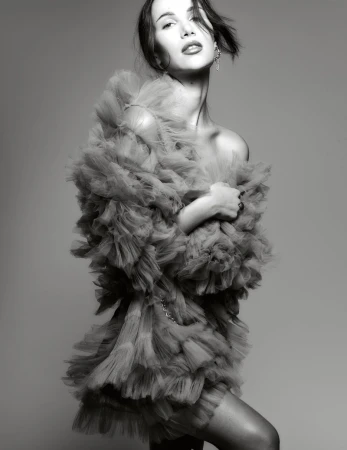 Model Maria Gutjahr poses in a dramatic voluminous ruffled tulle mini dress against a neutral studio backdrop in black and white.