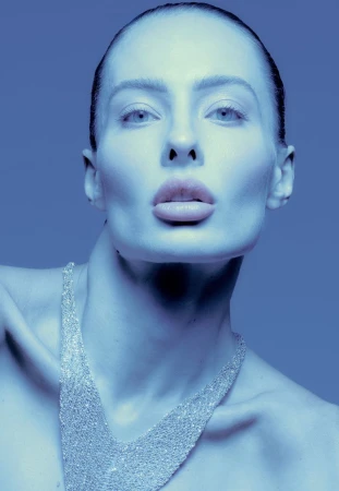 Close-up portrait of a female model wearing a sparkly V-neck necklace under cool blue lighting for L'Officiel Baltics.