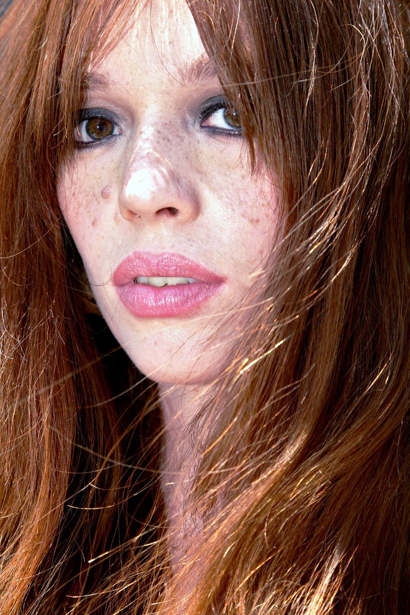 Close-up portrait of a red-haired adult female with fair skin and freckles, shot with a shallow depth of field and natural lighting.