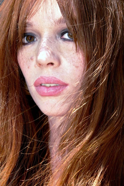 Close-up portrait of a red-haired adult female with fair skin and freckles, shot with a shallow depth of field and natural lighting.