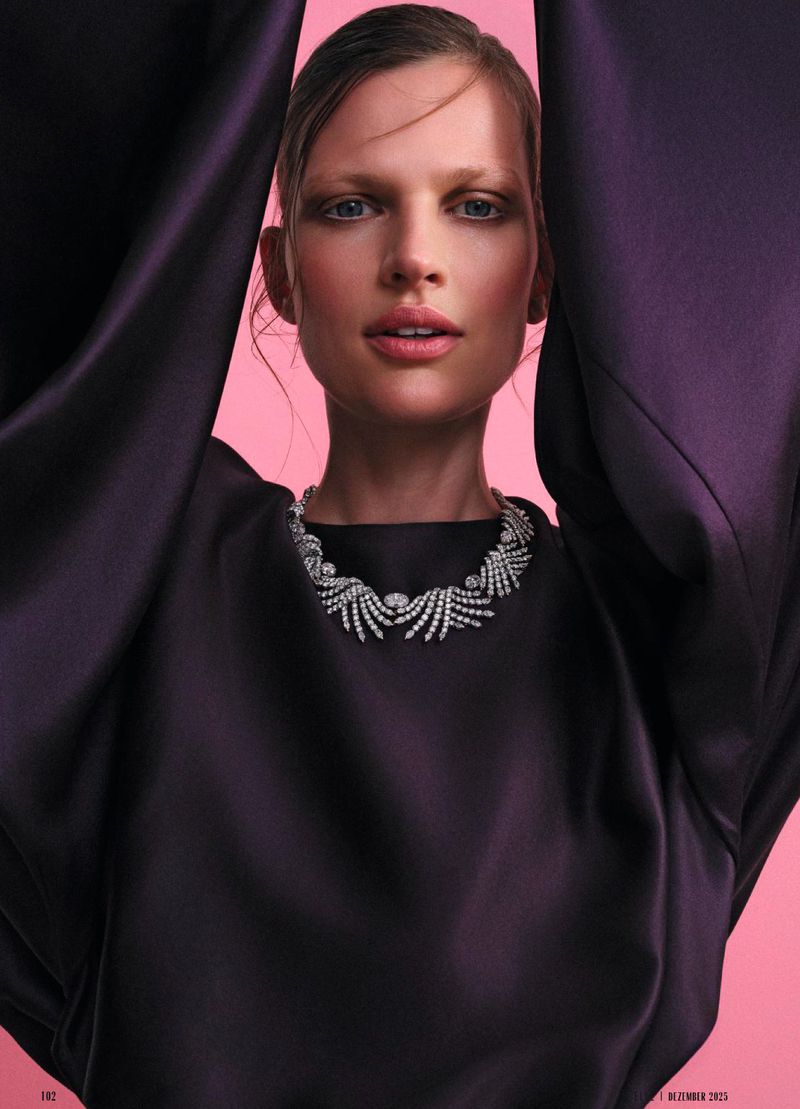 Elegant woman poses in a black dress and statement necklace in a fashion style portrait with soft pink background for a fashion ad.