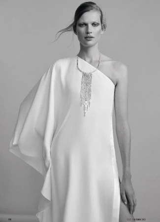 Model Bette Franke wearing a white one-shoulder dress and crystal necklace in a studio portrait for Elle Germany.