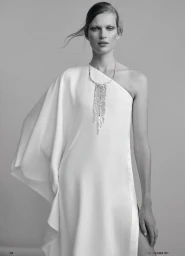 Model Bette Franke wearing a white one-shoulder dress and crystal necklace in a studio portrait for Elle Germany.