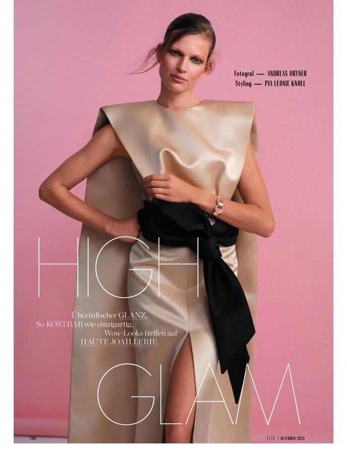 Model Bette Franke wearing a champagne satin structured gown with a black sash against a pink studio backdrop for Elle Germany.