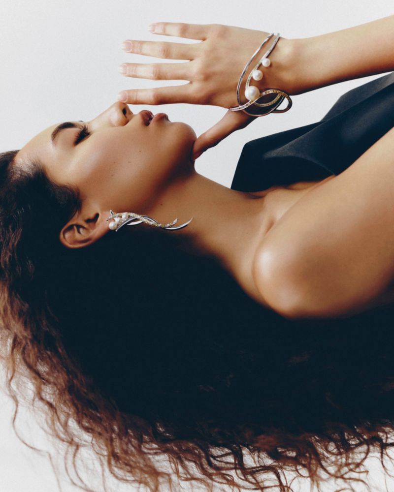 Model Morgan Fernandez in profile wearing a sculptural pearl cuff bracelet and silver earring against a white background.