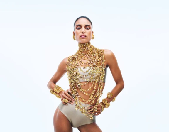Model wearing elaborate layered gold crystal jewelry and matching bracelets against a clean white background.