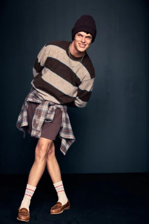Model in striped sweater and beanie leaning forward playfully against a dark grey background for Abercrombie and Fitch