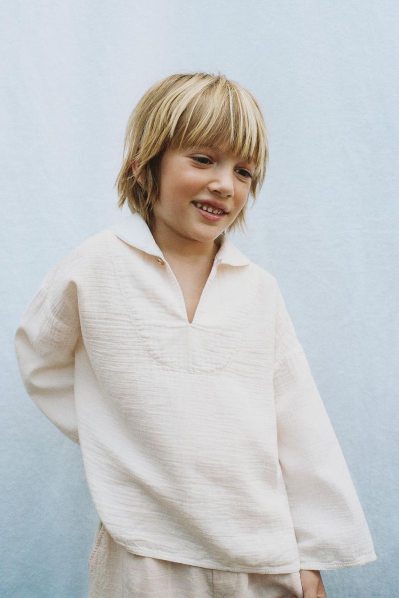 Portrait of a young boy with blonde hair wearing a collared shirt, captured in an indoor setting with soft lighting.