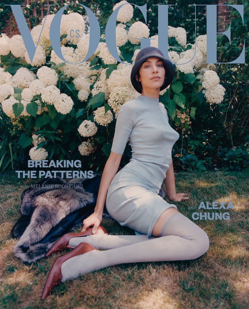 Vogue cover featuring a woman in light blue outfit and a hat, sitting on the grass in front of white flowers. The cover also features text elements.