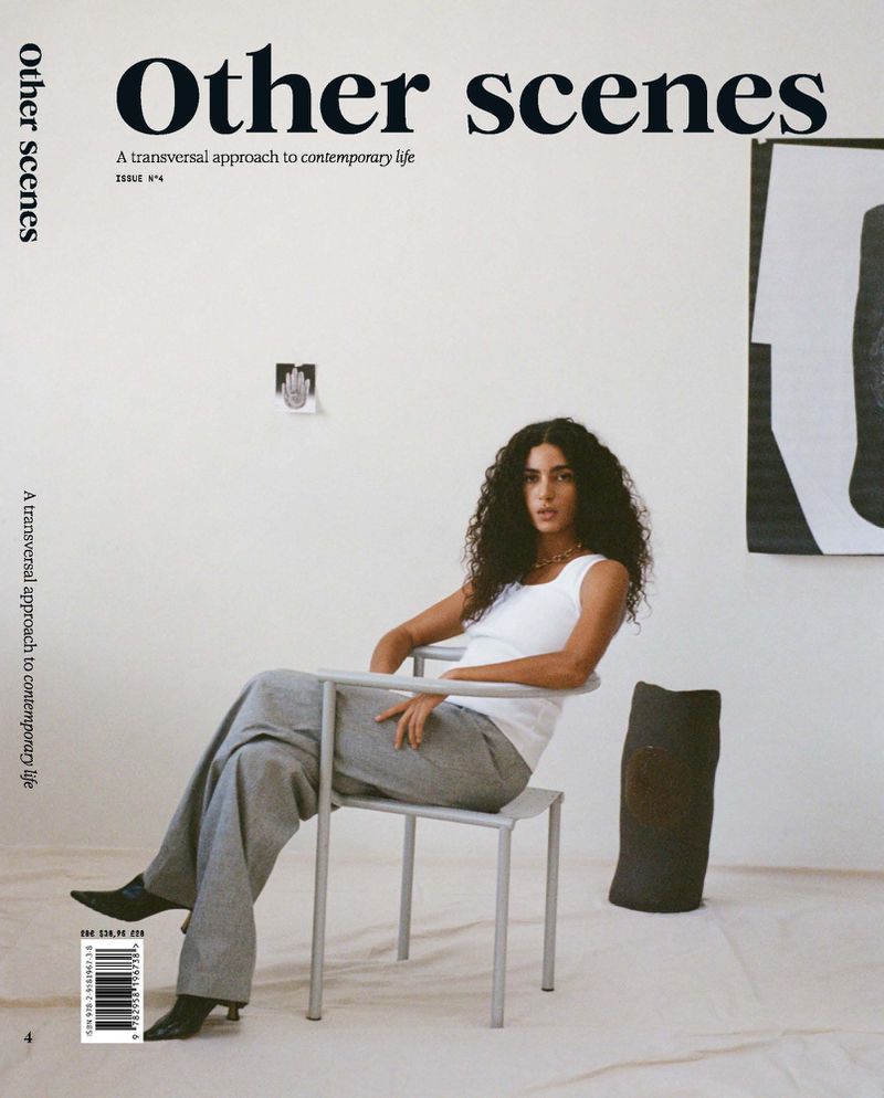Magazine cover featuring a woman with curly hair, sitting on a chair in front of a white wall with black and white modern art.