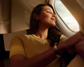 Woman in yellow top looking out an airplane window in warm natural light by photographer Saskia Wilson