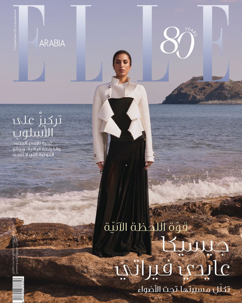 Elle Arabia cover featuring Aïda Mouaddab standing on a rocky beach in a black dress and cream jacket with the ocean and sky in the background.