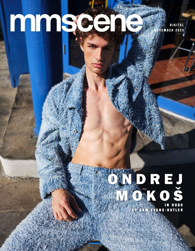 Magazine cover featuring a male model wearing a blue textured outfit, posing with one arm raised against a blue doorway.
