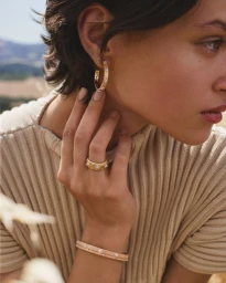 Close-up of a woman wearing gold hoop earrings, a matching gold ring, and bangles for Buccellati Fall Edit campaign.