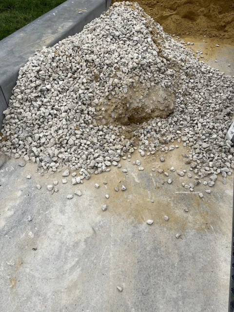 Pile of gravel with sand on a concrete surface. The gravel is small, angular and mostly white in color, creating a rough texture.