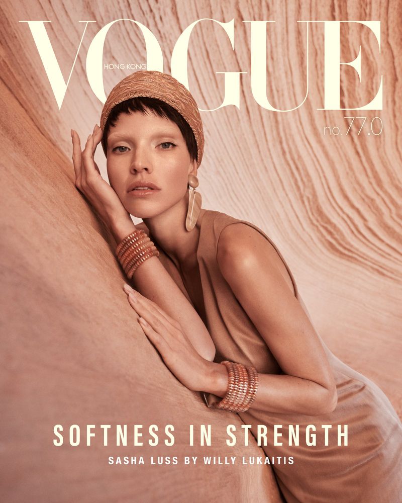 Vogue Hong Kong cover featuring Sasha Luss in a tan dress and straw hat, leaning against a textured backdrop. Close-up shot, neutral tones.