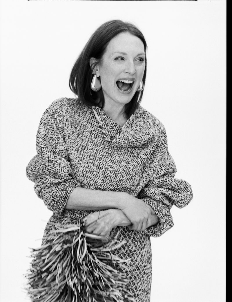 Black-and-white portrait of an adult female with short hair laughing, wearing patterned top and silver earrings, holding a feathered object.