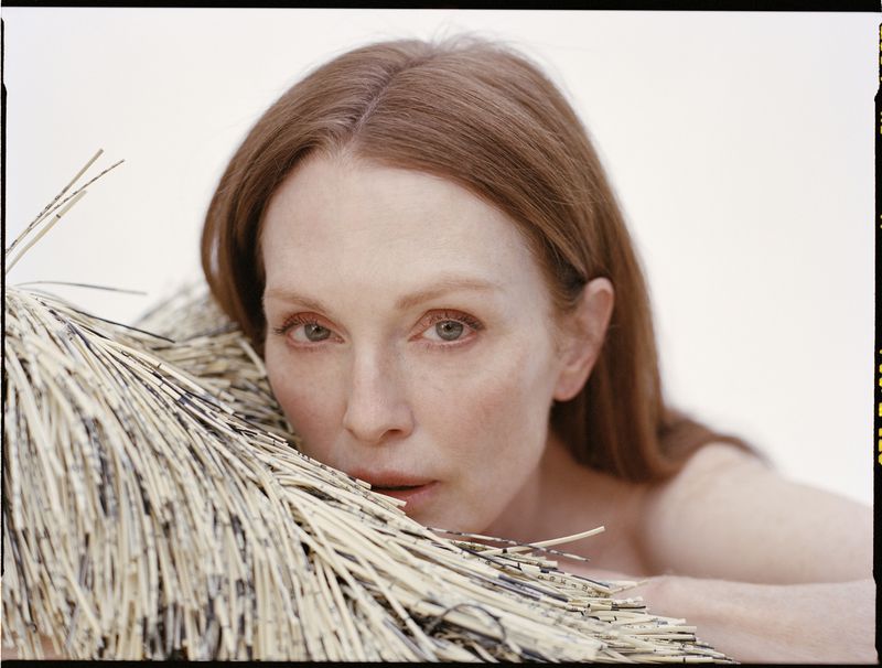 Portrait of an adult woman with red hair, fair skin, and green eyes, with a neutral expression, next to a bundle of dry straw.