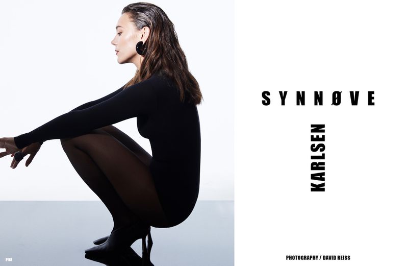 A woman in a black bodysuit crouches in a studio, photographed with bright lighting beside bold text, showcasing a modern and minimalist aesthetic.