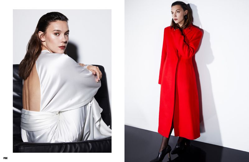 Fashion editorial shot featuring a woman in a backless silver gown seated and another woman in a bright red coat against a clean backdrop.