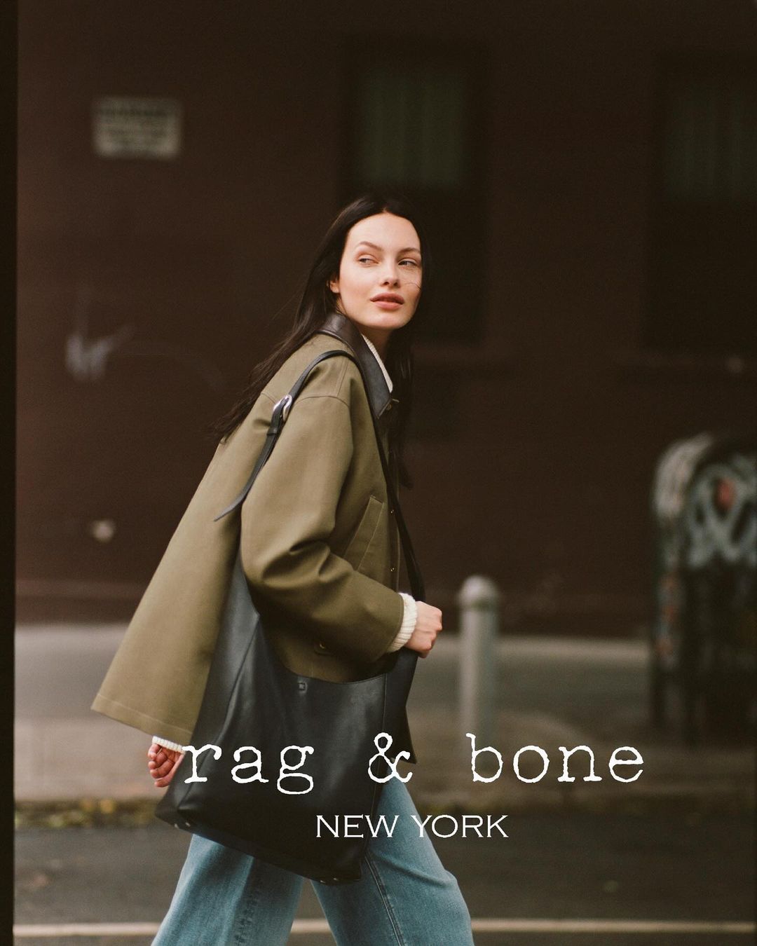A woman in an olive jacket walks outdoors, carrying a black leather bag, styled for Rag & Bone against an urban background.