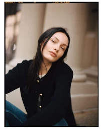 Portrait of a woman with dark hair wearing a black cardigan and blue jeans outdoors against classical architecture