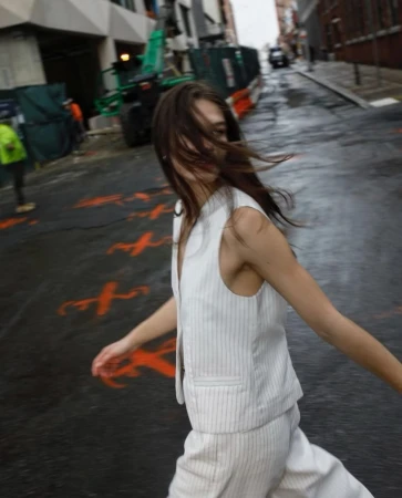 Woman in pinstripe suit walks on a wet city street near construction equipment; blurred motion and urban environment.