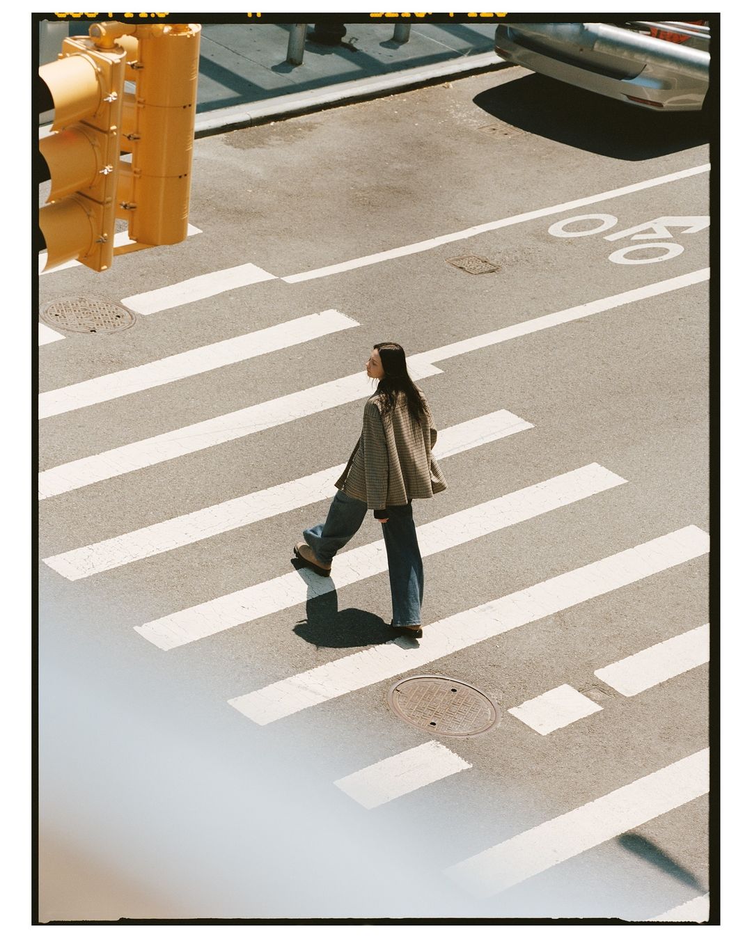 Woman in casual clothing crosses a zebra striped crosswalk with a traffic light and road markings in an urban outdoor setting.