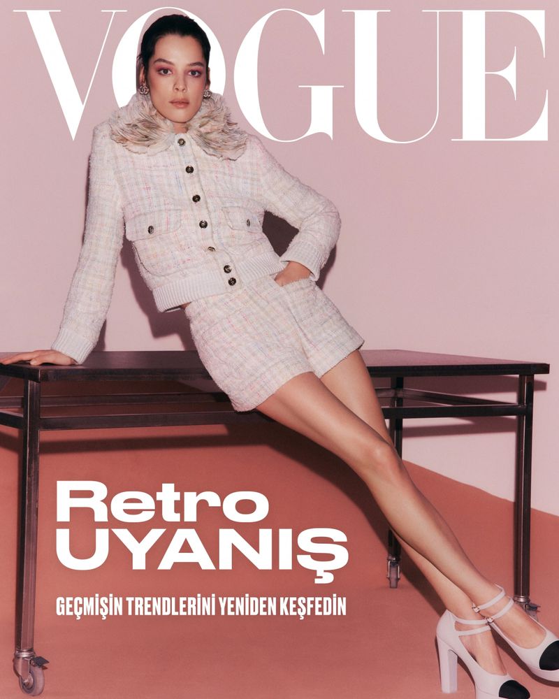 Vogue cover featuring a woman in a tweed jacket and shorts, posing on a table against a pink background in a fashion editorial shot.