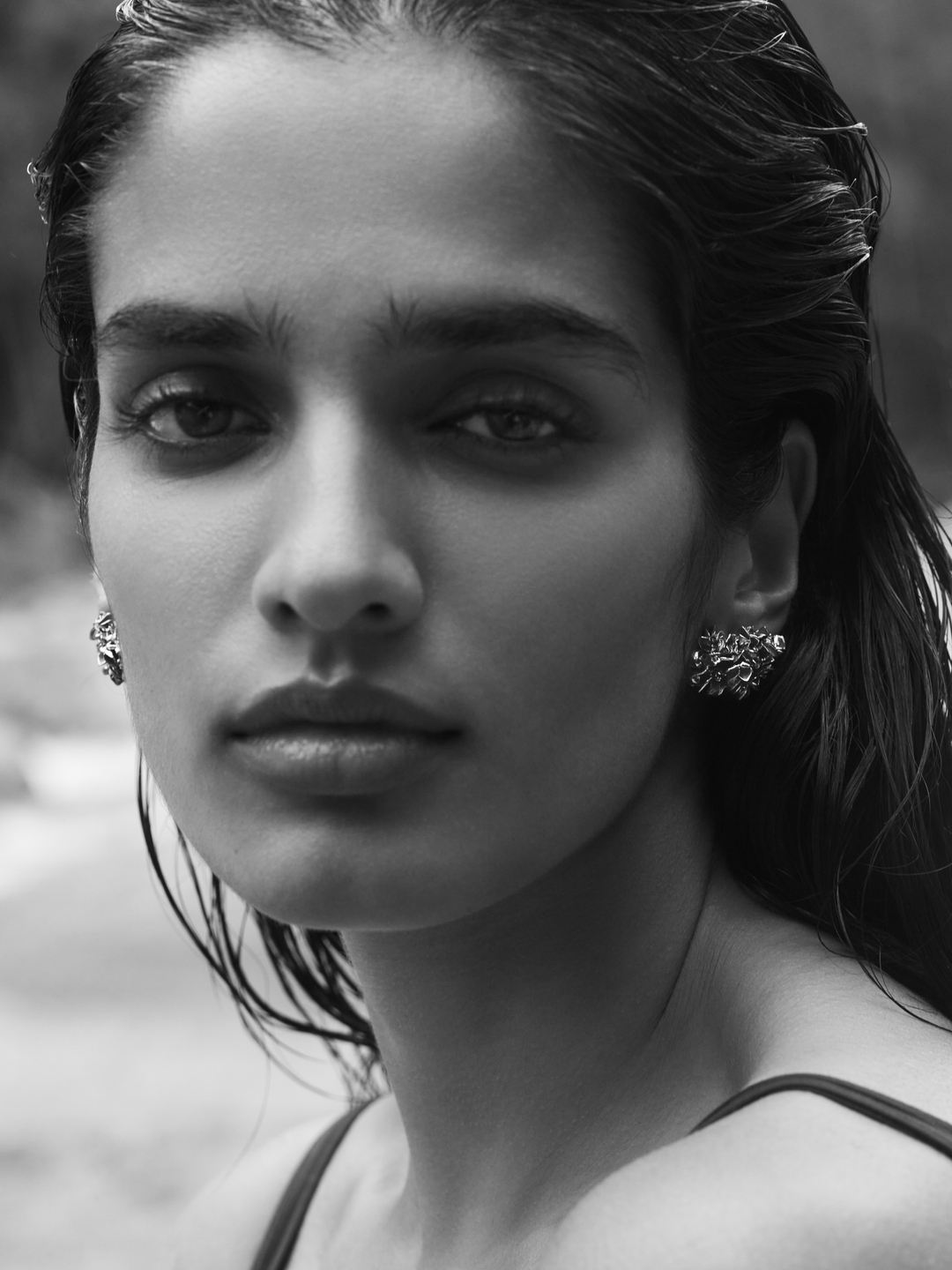 Close-up black and white portrait of a woman wearing detailed earrings with wet hair pulled back