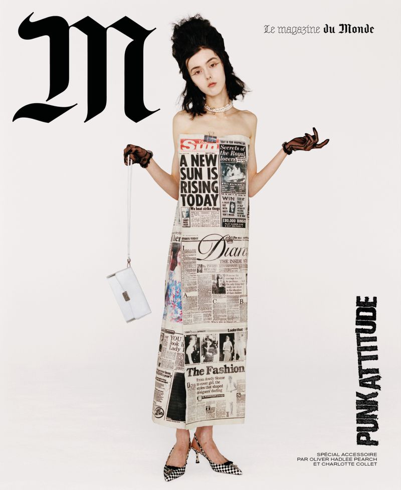 Fashion editorial shot of a pale-skinned woman with dark hair in a newspaper print dress, accessorized with gloves, purse, and heels.