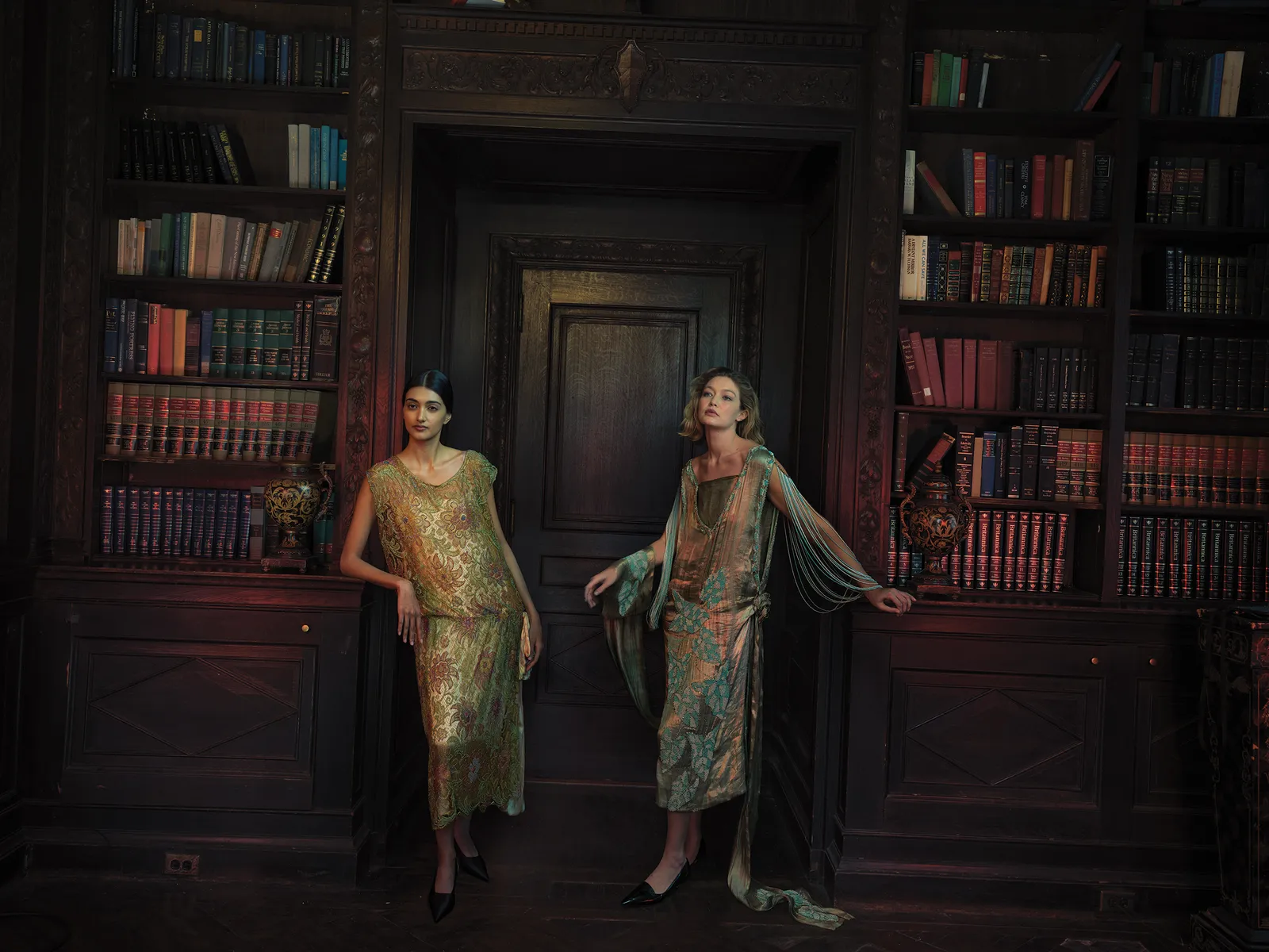Two women pose in flapper-style dresses inside a wood-paneled room with bookshelves. The lighting gives the scene a vintage-era mood.