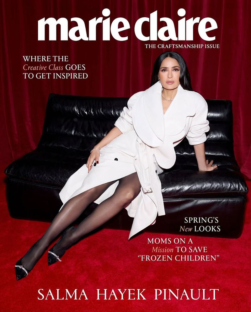 Salma Hayek Pinault poses on a black leather couch against a red curtain for a Marie Claire cover, wearing a white coat and black pantyhose.