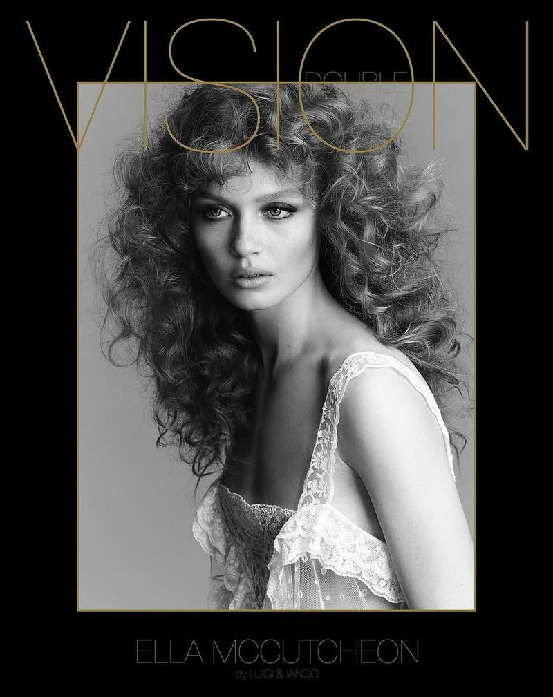 Black and white portrait of Ella McCutcheon with large curly hair and a semi-transparent lace top in front of a black background.