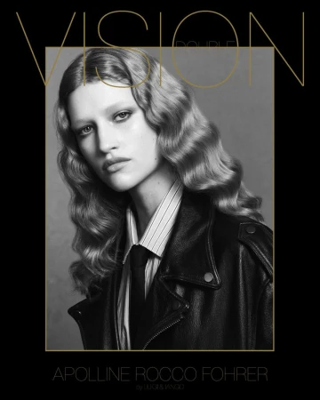 Monochrome portrait of a model with wavy hair, wearing a striped shirt, tie, and black leather jacket, against a grey backdrop.