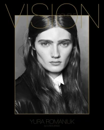 Monochrome portrait of model Yura Romaniuk with long dark hair wearing a white collar shirt and black jacket.