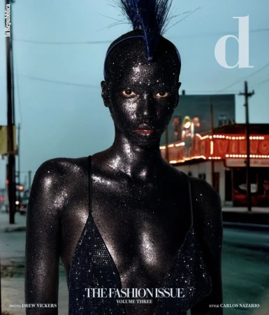 Fashion magazine cover featuring a model with black glittering skin, posing in front of a city street at dusk.